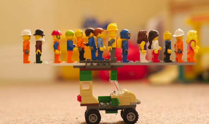Lego people standing in a line on top of a lego car.