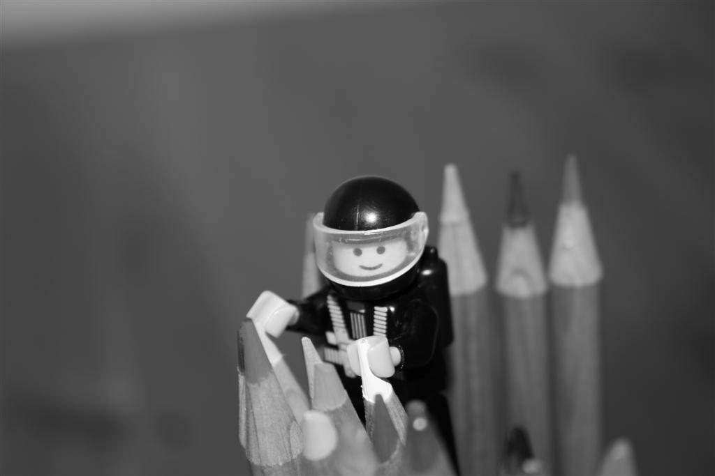 A lego character holding on to the edge of two pencils.