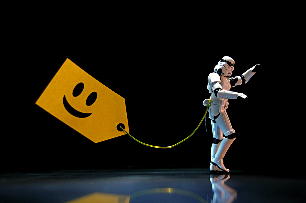 A storm trooper is on the right-hand side of the screen pointing to something that we can't see. There is a yellow tag with a smiley face on the left hand side of the screen with a piece of string that comes off of it that is tied to the storm trooper's waist.